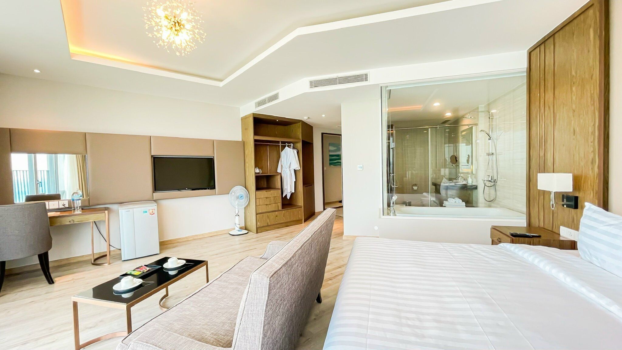 Een moderne hotelkamer met een groot bed, een bureau met een flatscreen televisie, een inloopkast en een douchecabine met glazen wanden.