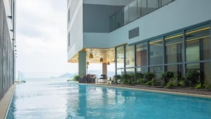 Une piscine avec vue sur la mer, un espace extérieur aménagé et couvert, et une façade de bâtiment moderne.