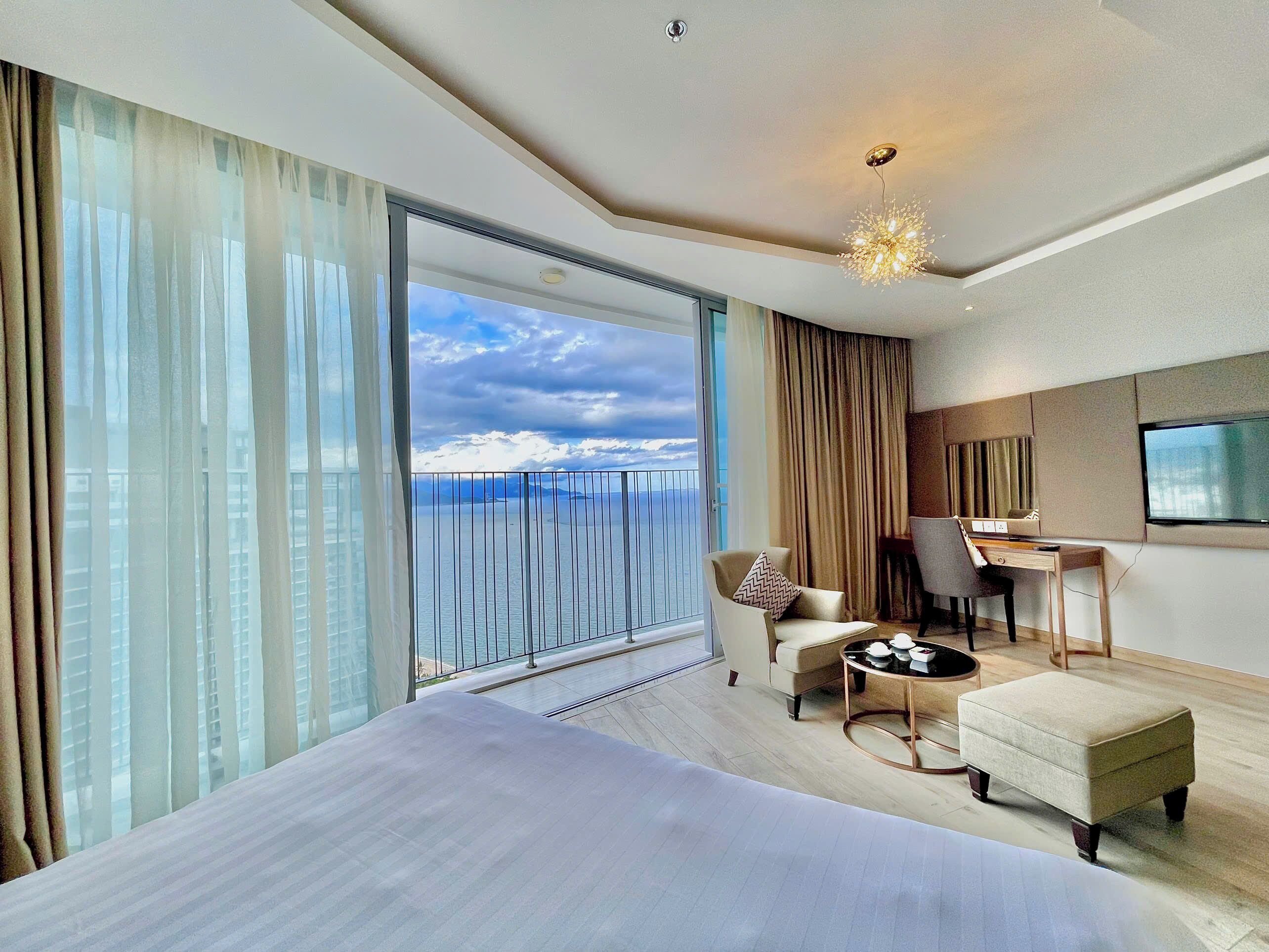 Quarto de hotel moderno com uma cama grande, uma escrivaninha, uma cadeira e vista para o mar.
