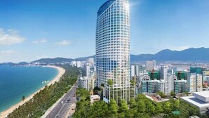 Un immeuble moderne de grande hauteur, doté d’une façade incurvée, situé près d’une zone côtière, avec une plage et des montagnes en arrière-plan.