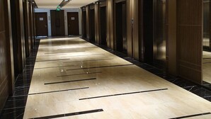 Un long couloir doté d’un sol en marbre poli, de portes en bois et d’un plafond pourvu d’un éclairage encastré.
