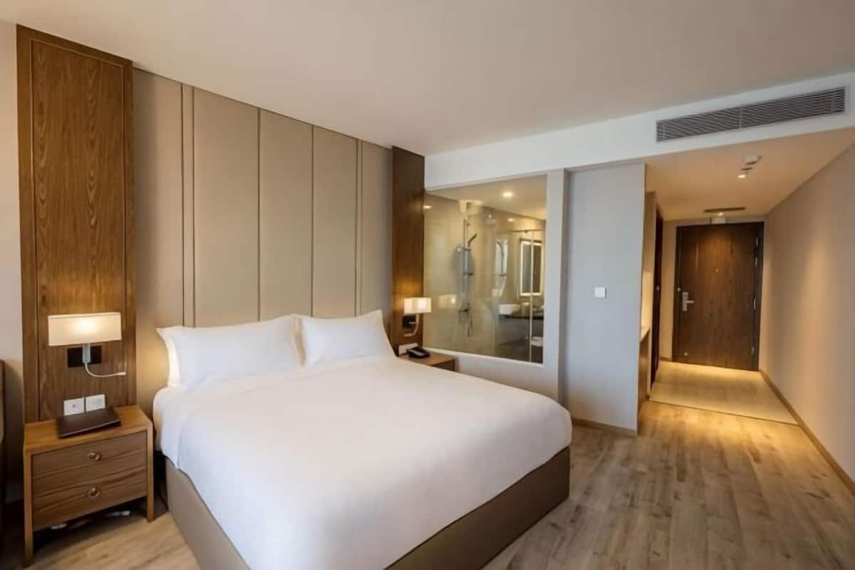 A hotel room with a large bed, bedside tables, a mirror, and a wooden wardrobe.