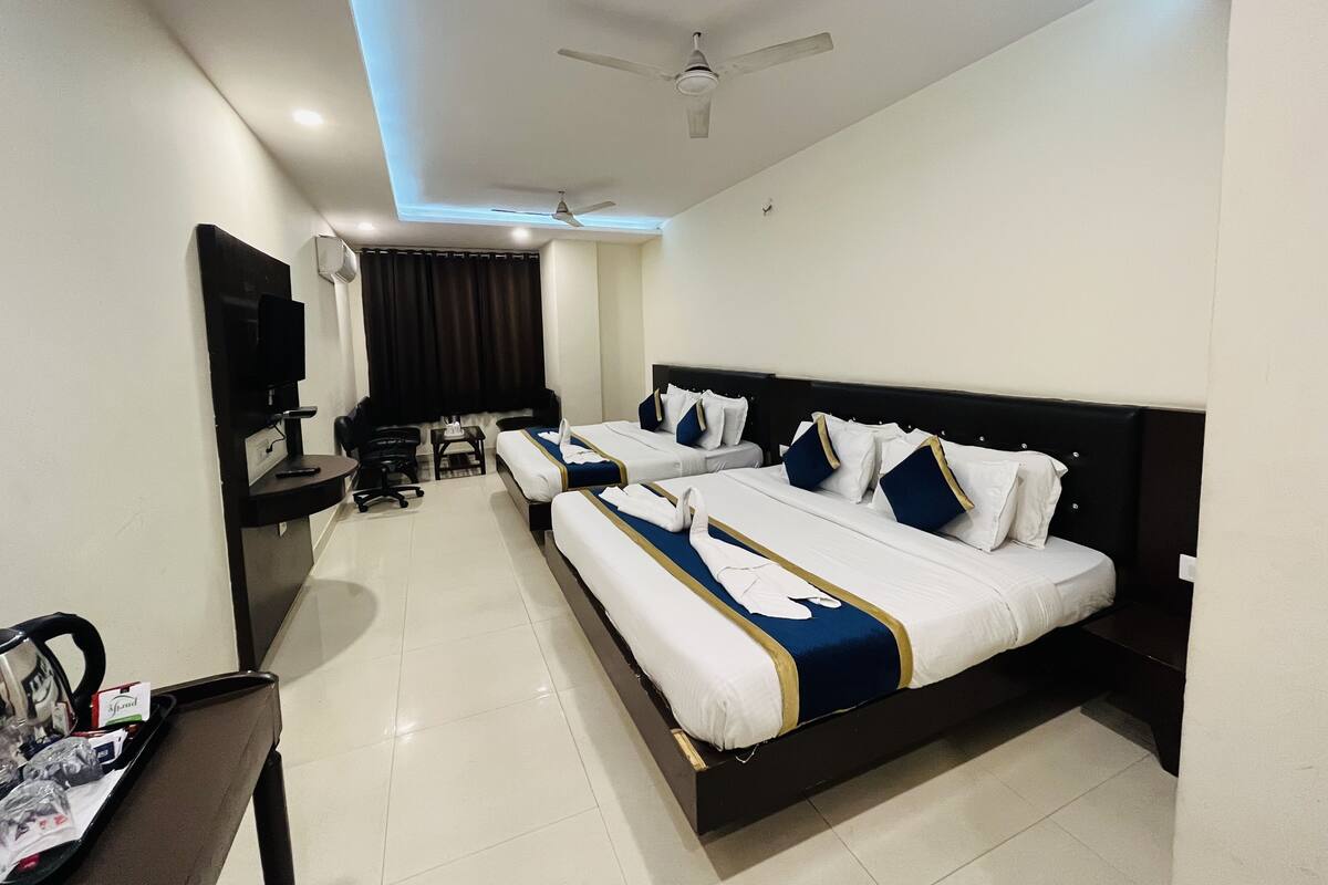Quarto de hotel com duas camas, uma escrivaninha, uma cadeira, uma televisão e um ventilador de teto.