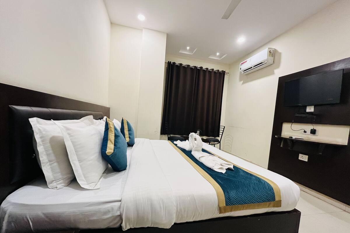 Quarto de hotel com cama, televisão de tela plana, ar-condicionado e um suporte de TV com controle remoto.