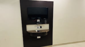 A wall-mounted TV with a control panel below it, a power outlet, and a small shelf. - Hotel City Heritage Haridwar (Haridwar)