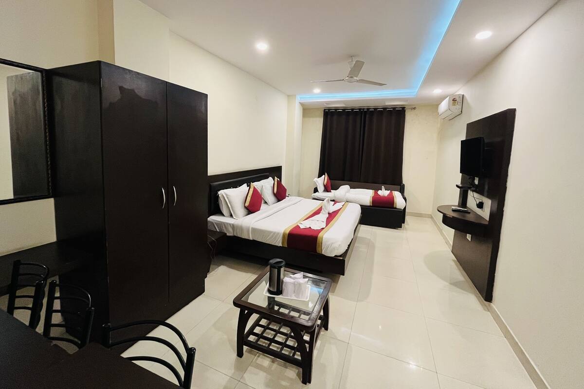Quarto de hotel com cama, escrivaninha, cadeira, televisão e ventoinha no teto.