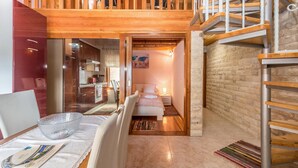 Une chambre d’hôtel chaleureuse avec un escalier en bois, une petite kitchenette et un lit agrémenté d’un tapis aux couleurs vives.