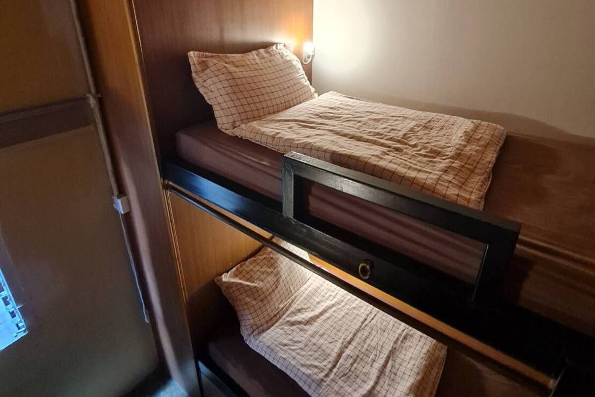 A compact room with a bunk bed, a small desk, and a wall-mounted light.