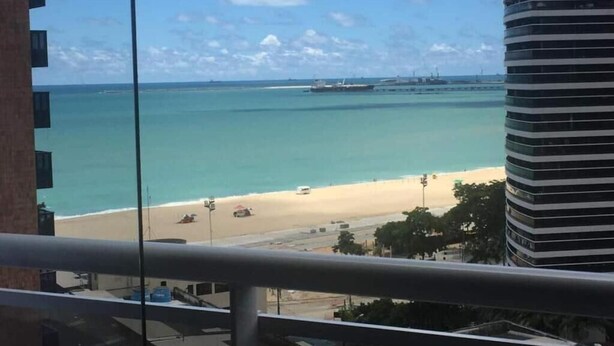 A view of a beach from a balcony with a clear sky, a sandy shore, and a large ship in the distance. - my way s flats (Fortaleza)