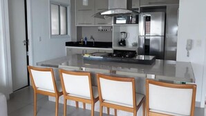 A modern kitchen with a central island, white cabinetry, stainless steel appliances, and three wooden chairs. - my way s flats (Fortaleza)