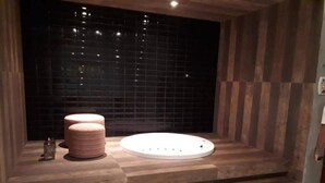 A spa area with a wooden bench, a white circular seating area, and a tiled wall. - my way s flats (Fortaleza)