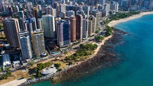 A coastal cityscape with high-rise buildings, a beach, and rocky shoreline. - my way s flats (Fortaleza)