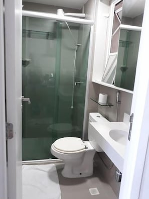 Un baño pequeño y moderno con ducha de vidrio, inodoro y lavamanos.