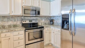 A kitchen with white cabinets, a stainless steel refrigerator, a microwave, a stove, and a coffee maker. - Sea Banks 204, Two Bedroom, Two Bathroom, Oceanfront (Garden City Beach)