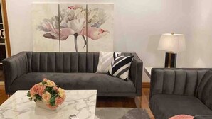 Una sala moderna con un sofá gris, una mesa de centro de mármol y un jarrón floral.