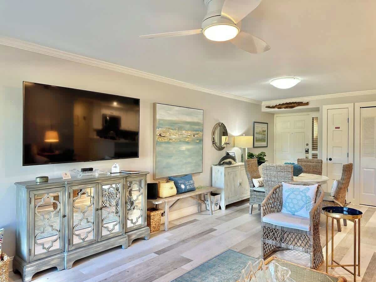 Un salon avec un téléviseur, des meubles en osier, un ventilateur de plafond et un grand tableau.