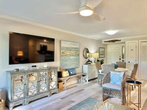 Un salon avec un téléviseur, des meubles en osier, un ventilateur de plafond et un grand tableau.