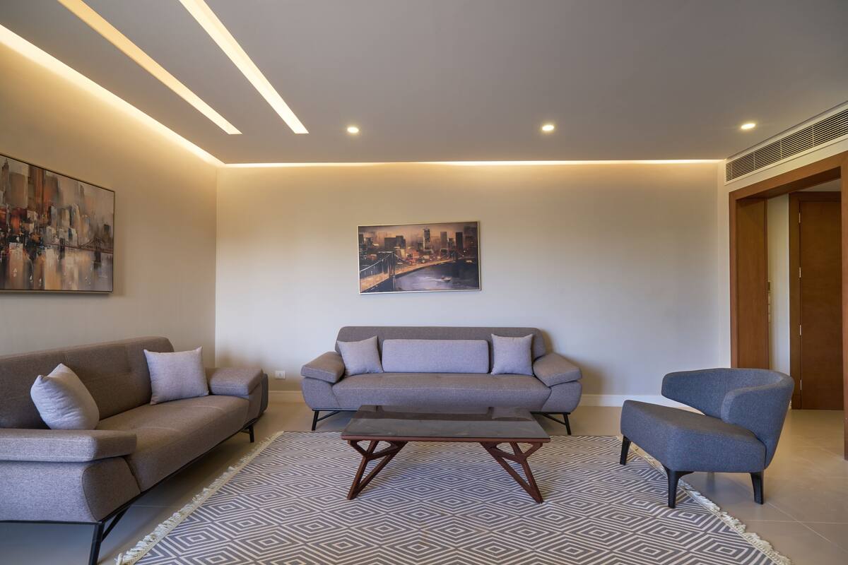 A modern living room with two sofas, a coffee table, and a painting of a cityscape.