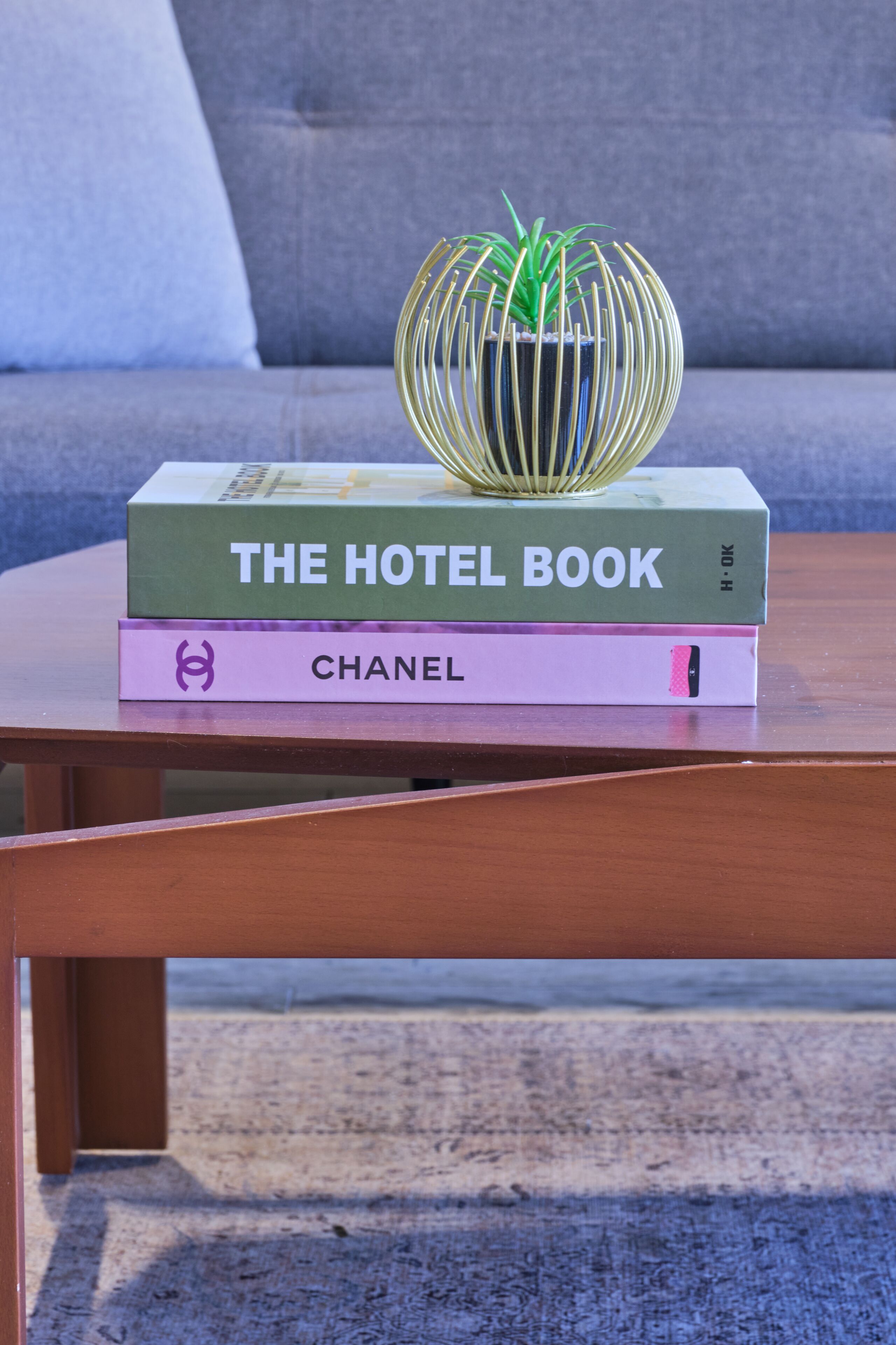 A stack of books on a wooden table with a decorative plant on top.