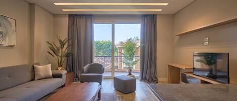A modern living room with a sofa, armchair, ottoman, wooden coffee table, and a flat-screen TV on a stand.