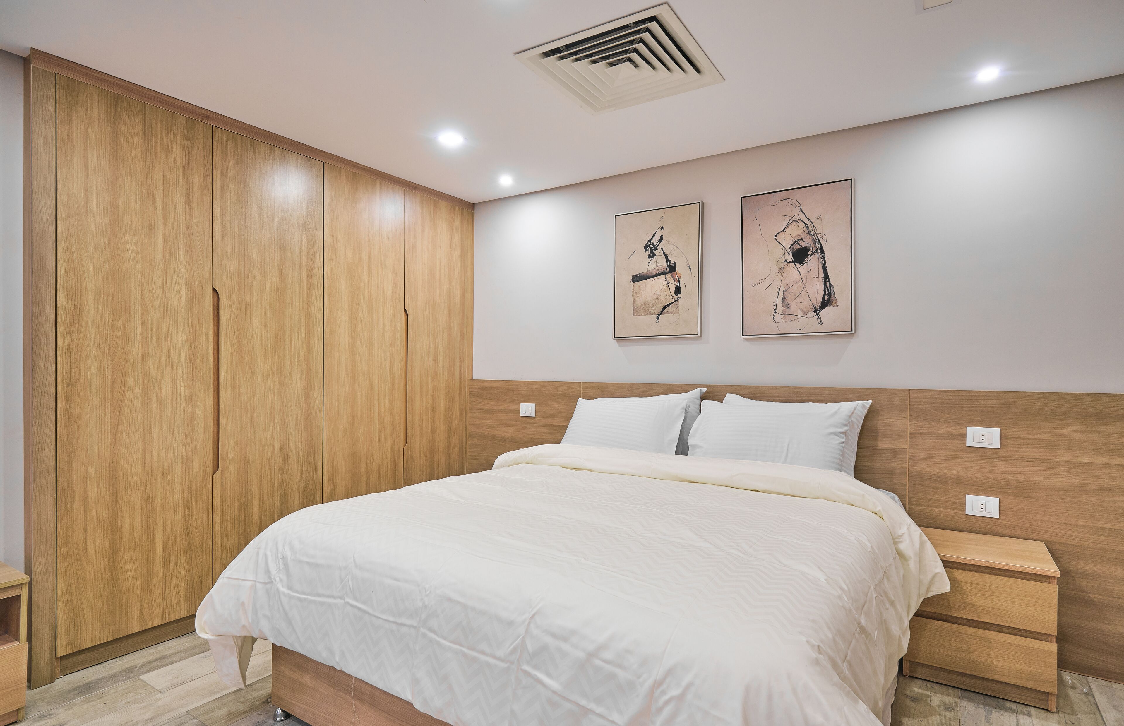Une chambre avec une grande armoire en bois, un lit avec une literie blanche et deux œuvres d’art accrochées au mur.