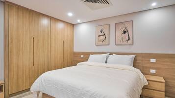 Une chambre avec une grande armoire en bois, un lit avec une literie blanche et deux œuvres d’art accrochées au mur.