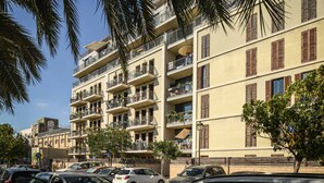 Un edificio de varios pisos con balcones, coches aparcados y palmeras.