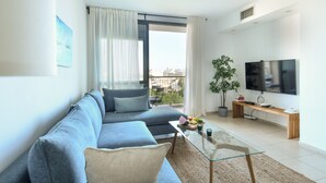 Un salón moderno con sofá, una mesa de centro de vidrio, televisor y balcón con vistas a la ciudad.