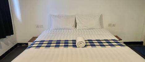 A hotel room with a neatly made bed, a checkered blanket, and a rolled towel on the bed.