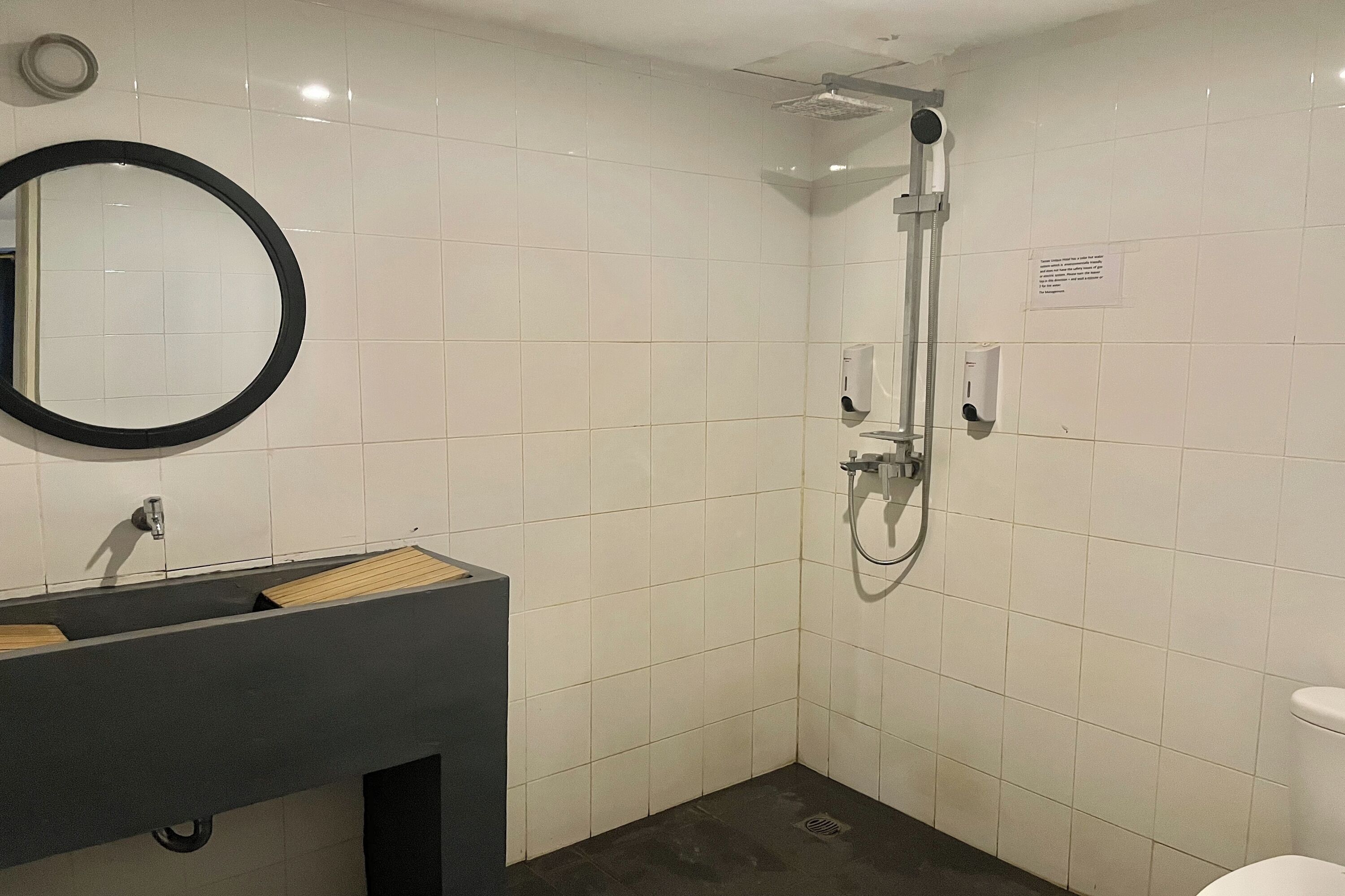 A modern bathroom with a dark sink, a round mirror, a handheld showerhead, and a toilet.