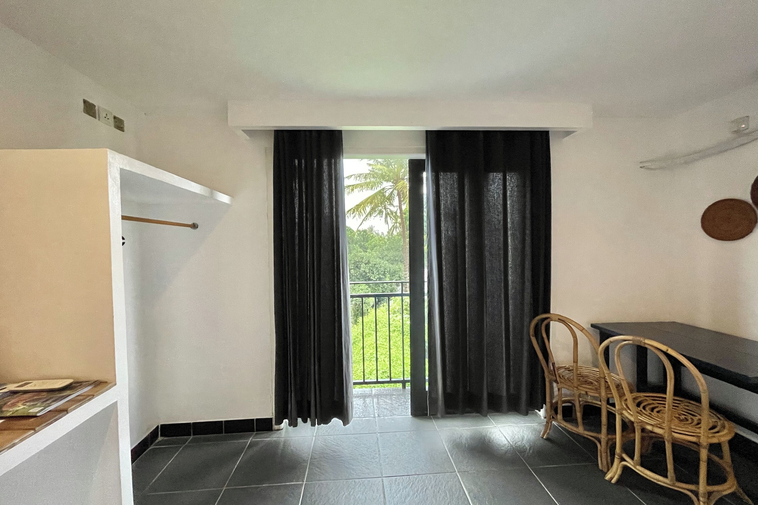 A room with a balcony, a table, two wicker chairs, and a black curtain.
