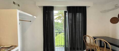 A room with a balcony, a table, two wicker chairs, and a black curtain.