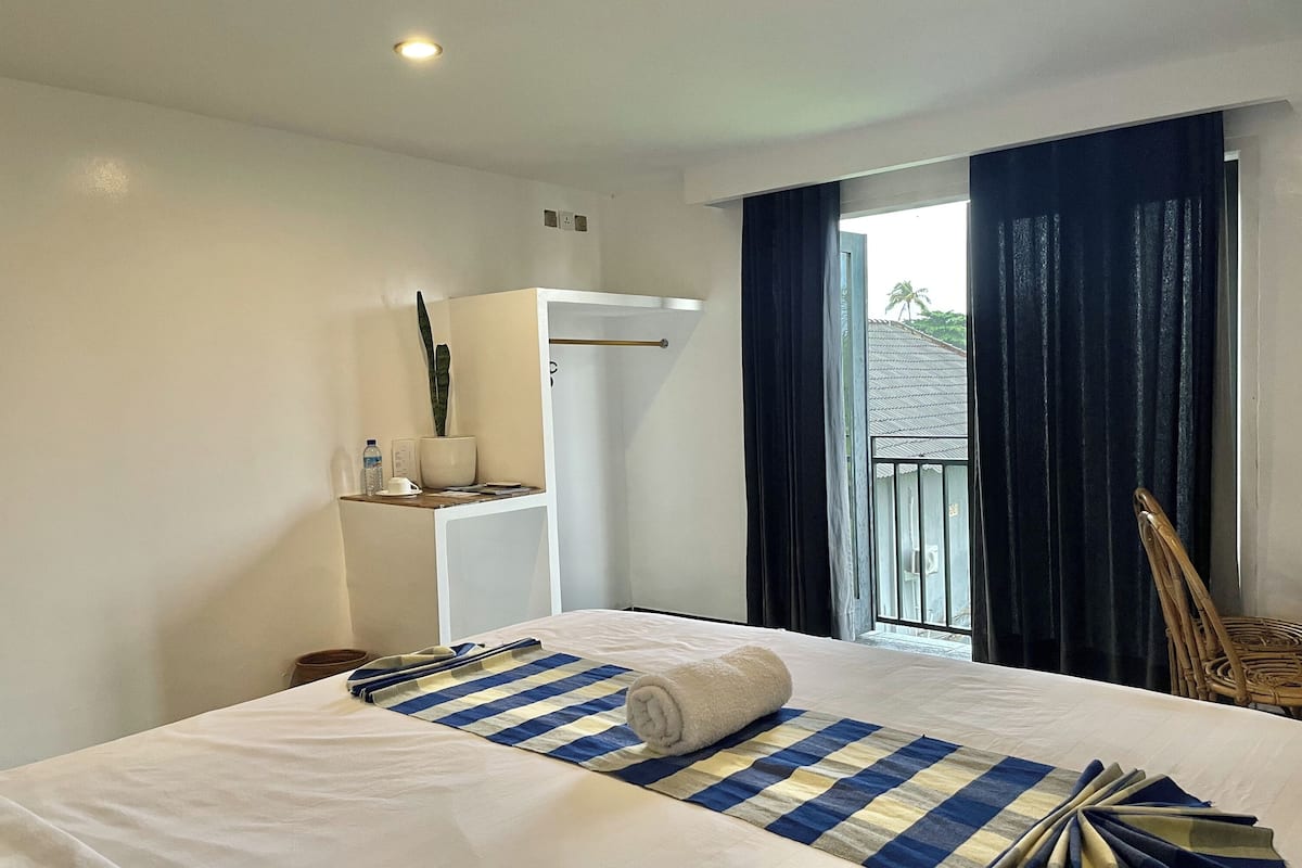 Habitación de hotel con cama, una mesita con una toalla, una silla, un armario y vistas al exterior.