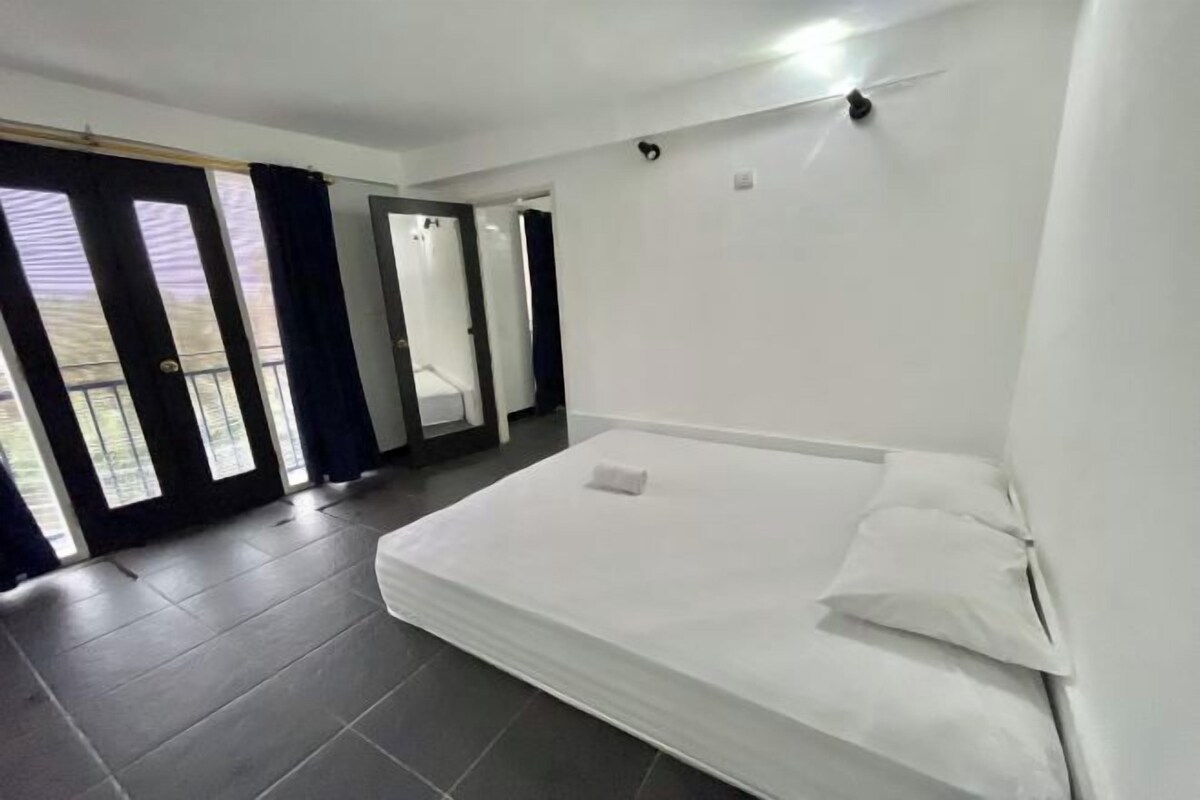 A modern hotel room with a large bed, a balcony with curtains, and a view of the outdoors.
