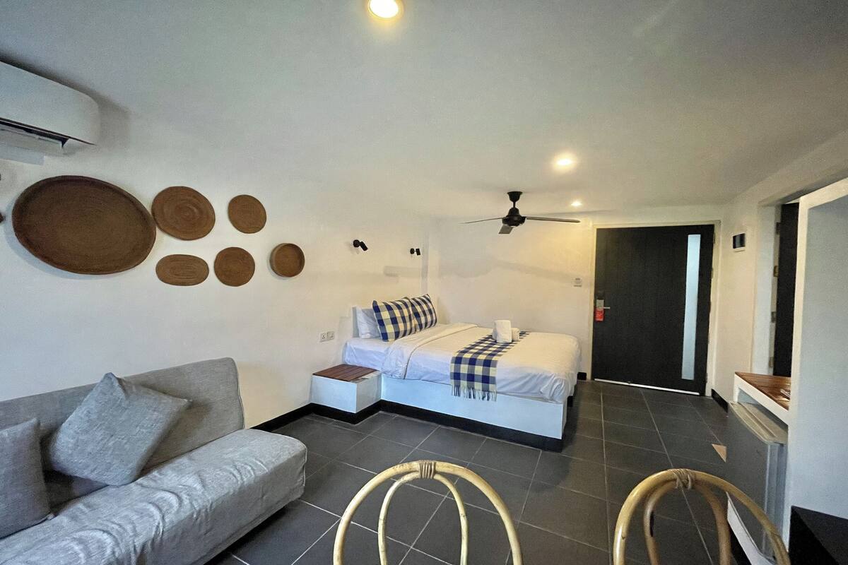 Una habitación de hotel con una cama, un sofá, un ventilador de techo y un aire acondicionado instalado en la pared.
