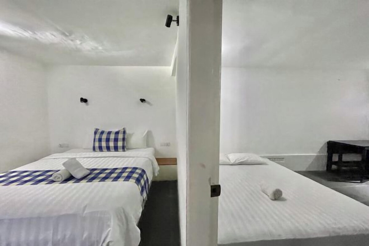 Habitación de hotel con dos camas, una mesita pequeña y un banco.