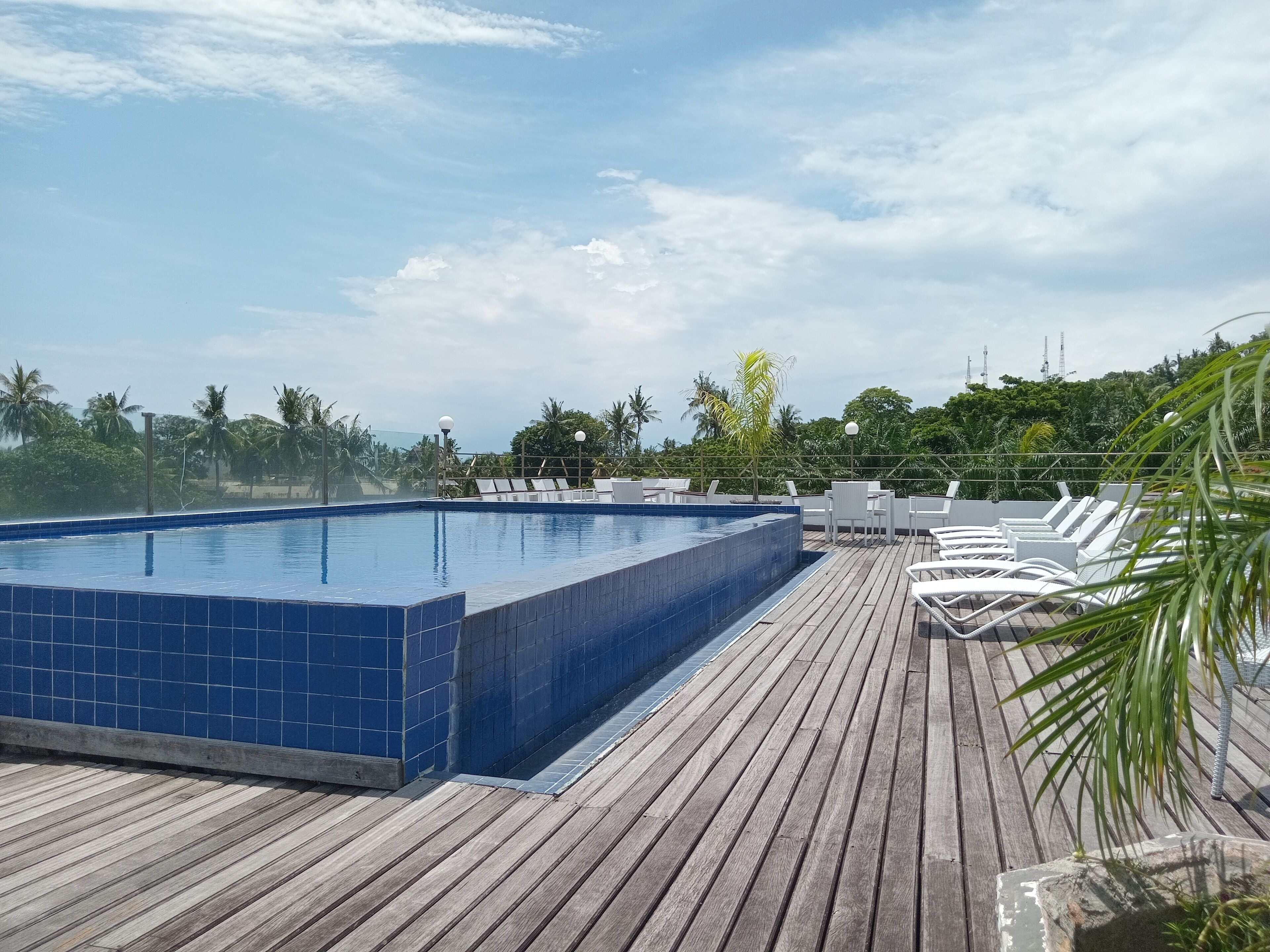Piscina no terraço com azulejos azuis, cercada por um deck de madeira e espreguiçadeiras brancas.