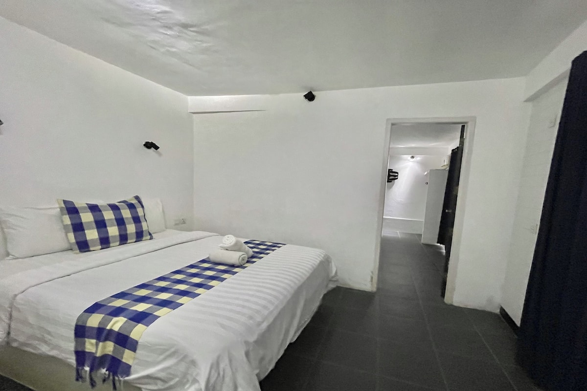 Un dormitorio con una cama, paredes blancas, una manta a cuadros y una toalla sobre la cama.