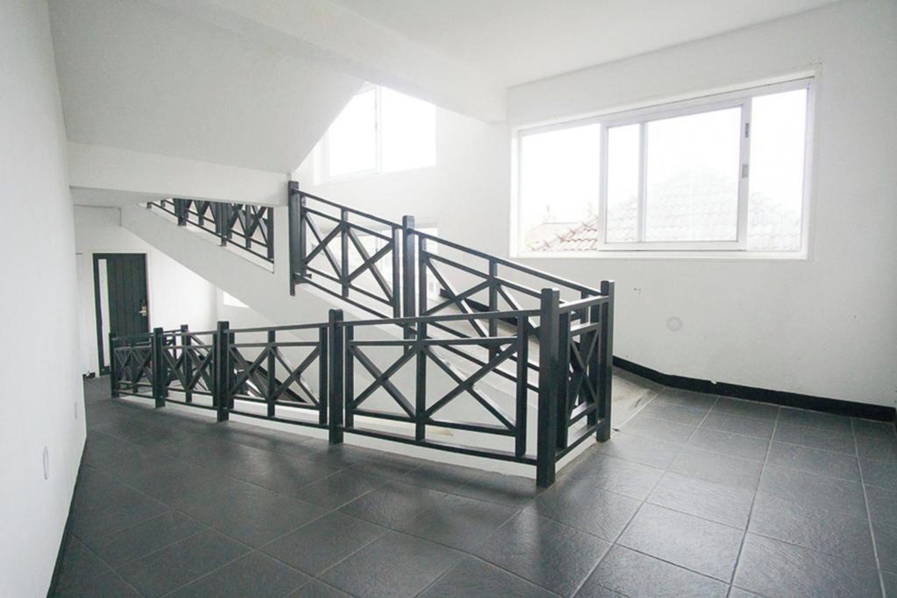 A staircase with a black metal railing in a room with white walls and a large window.