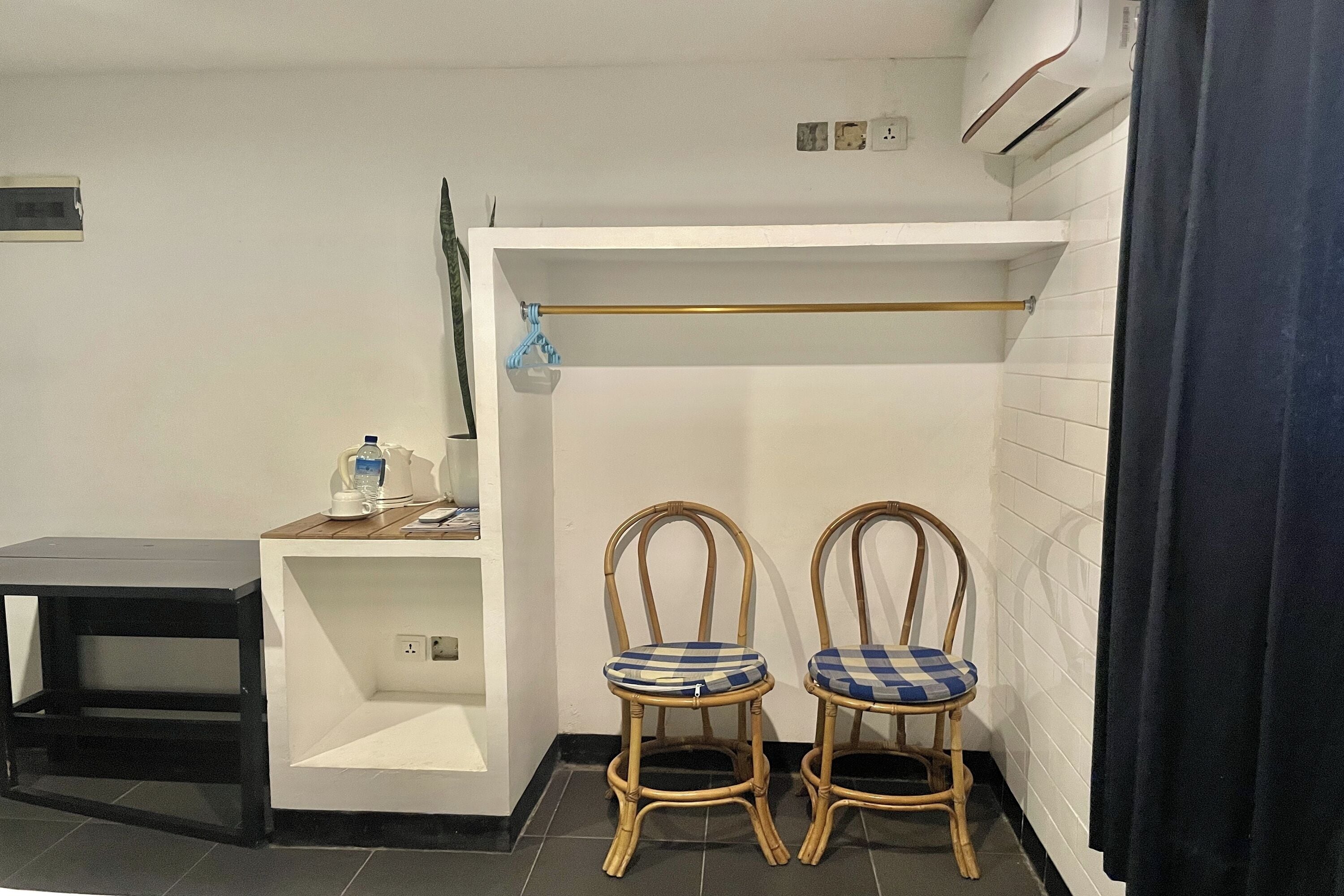 A small, clean room with two wicker chairs, a small table, and a shelf with a kettle and cups.