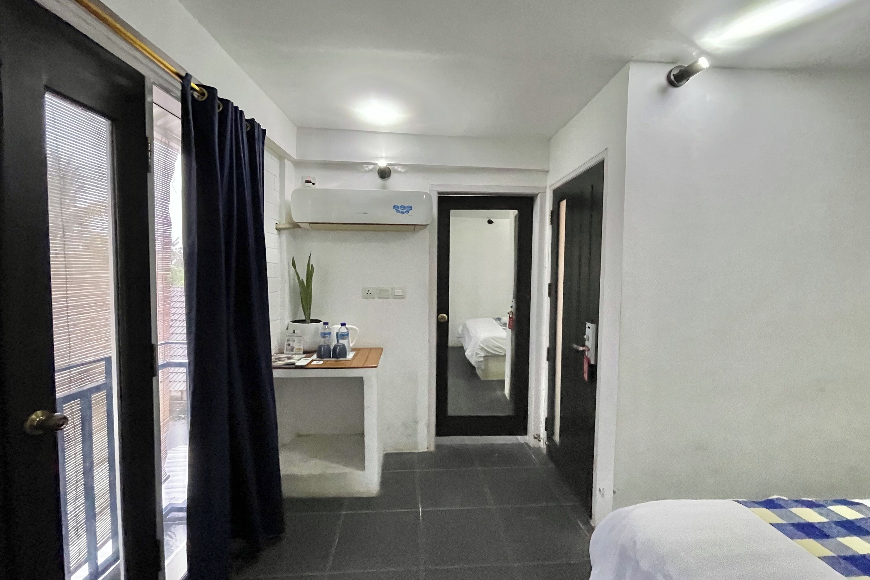 A hotel room with a bed, a desk with a potted plant, and a bathroom visible through an open door.