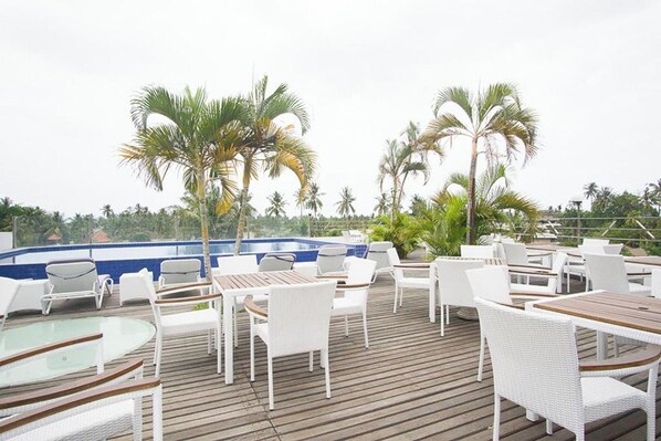 Una terraza con mobiliario de mimbre blanco, piscina y palmeras.