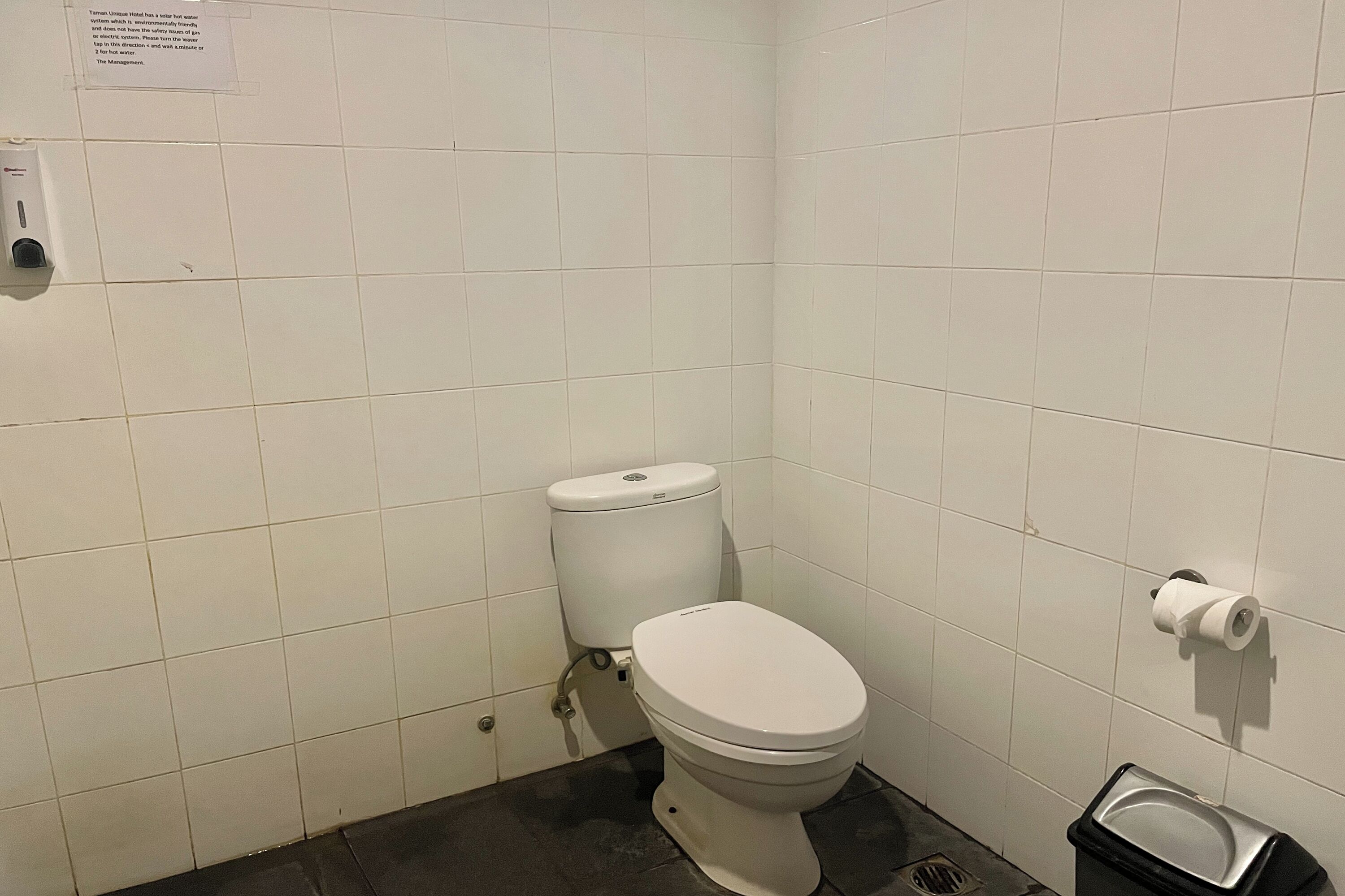 A small, clean bathroom with a toilet, a trash bin, and a paper towel dispenser.
