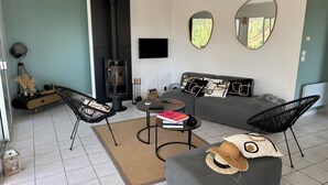 Een moderne woonkamer met een grijze bank, zwarte stoelen, een ronde salontafel en een open haard.