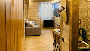 L’intérieur chaleureux d’un chalet avec un plancher en bois, un canapé, une table à manger et un téléviseur.