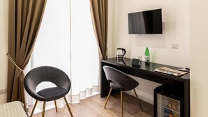 Ett modernt hotellrum med ett skrivbord, två stolar, en tv och en minibar.