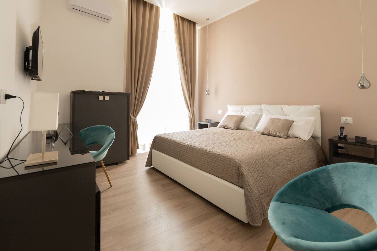 A modern hotel room with a bed, a desk, a chair, and a television.