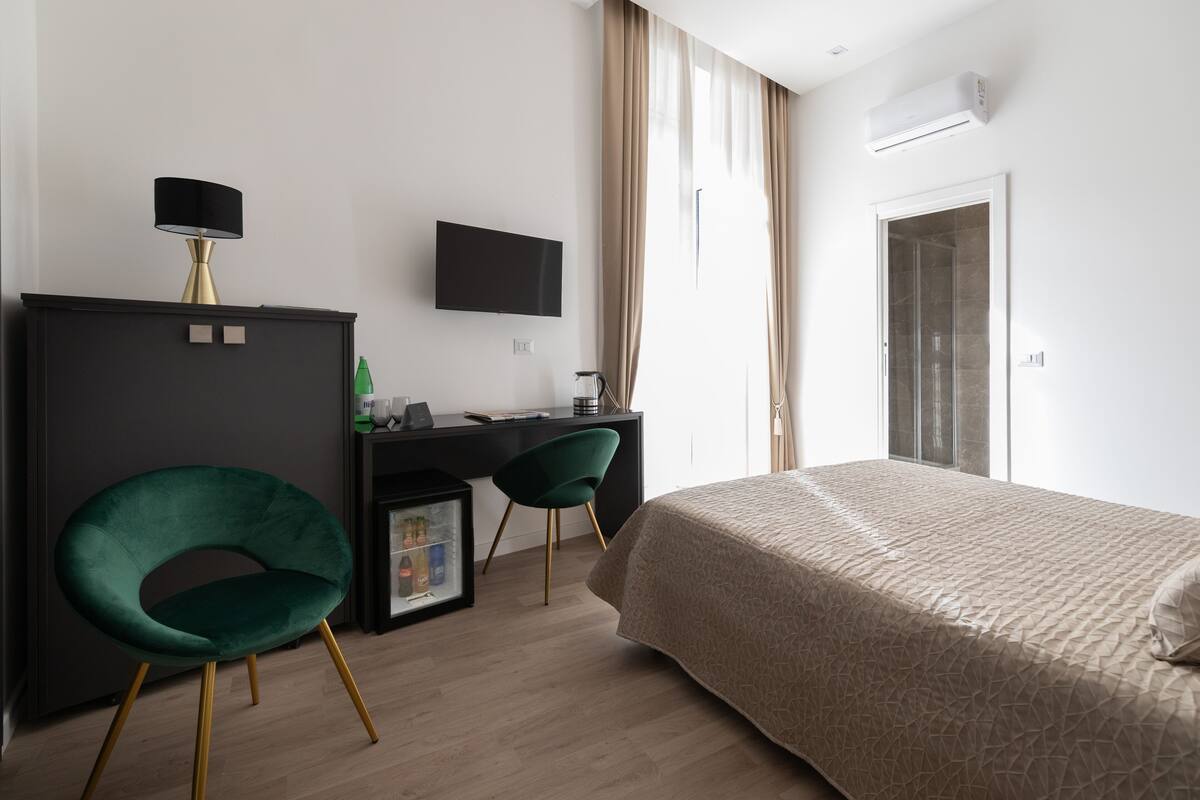 A hotel room with a bed, a desk with a computer, a TV, and a chair.