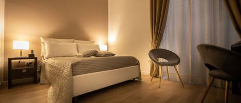 A bedroom with a bed, two bedside tables with lamps, a chair, and a large window with curtains.