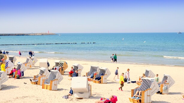 Een strand met rijen gestreepte strandstoelen en parasols, een zandstrand en een rustige zee.